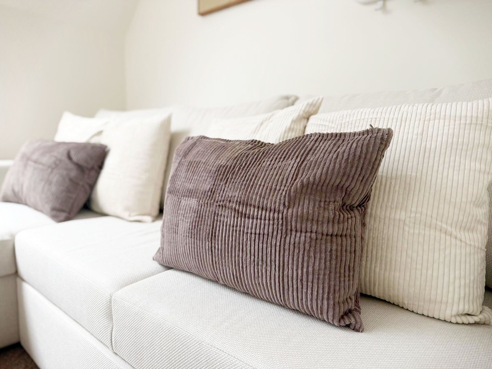 A white sofa with several cushions, including a ribbed one and a plain one.
