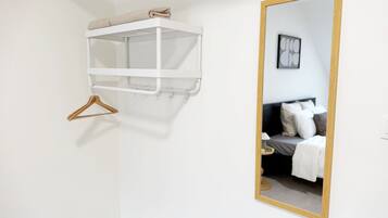 Una habitación blanca con una cama, un espejo de marco de madera y un estante blanco con una toalla.
