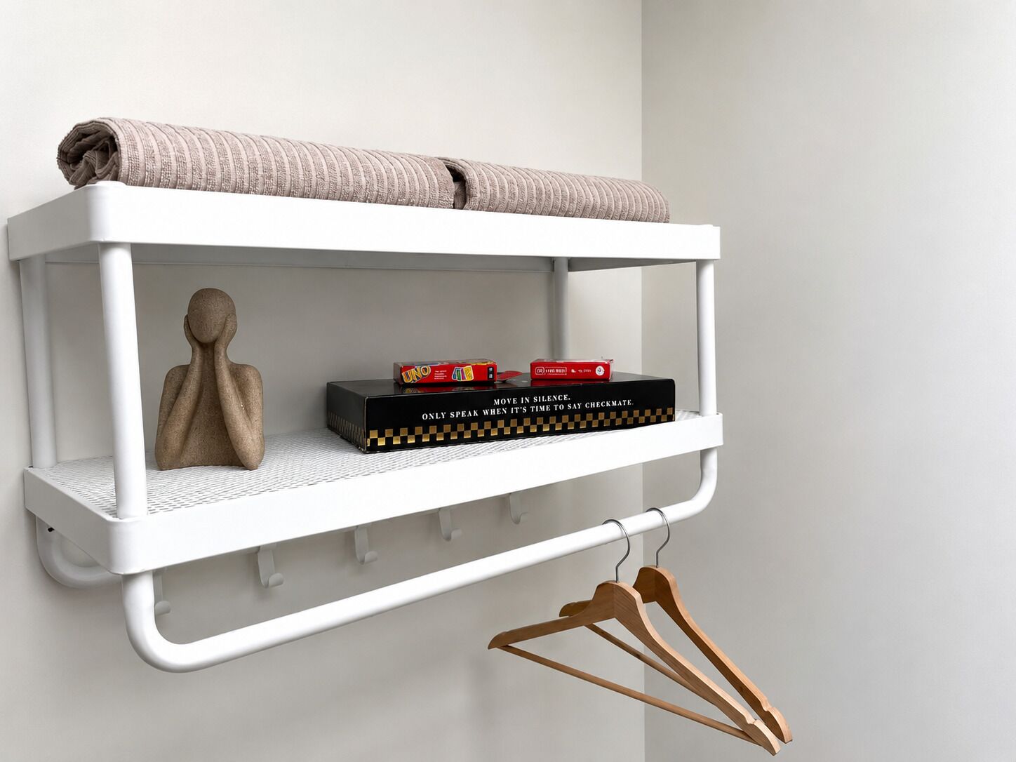 Een witte planken kast met een opgevouwen handdoek, een speldoos en een houten sculptuur.