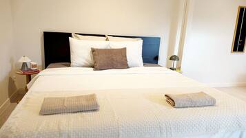 A neatly made bed with pillows, a bedside table with a lamp, and a door with a handle.