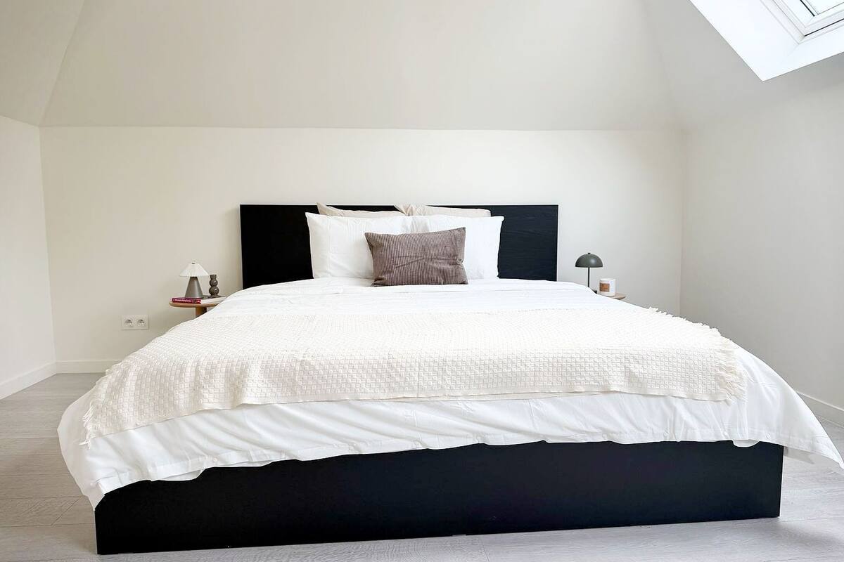Un dormitorio moderno con una cama grande, cabecera oscura y tragaluz.
