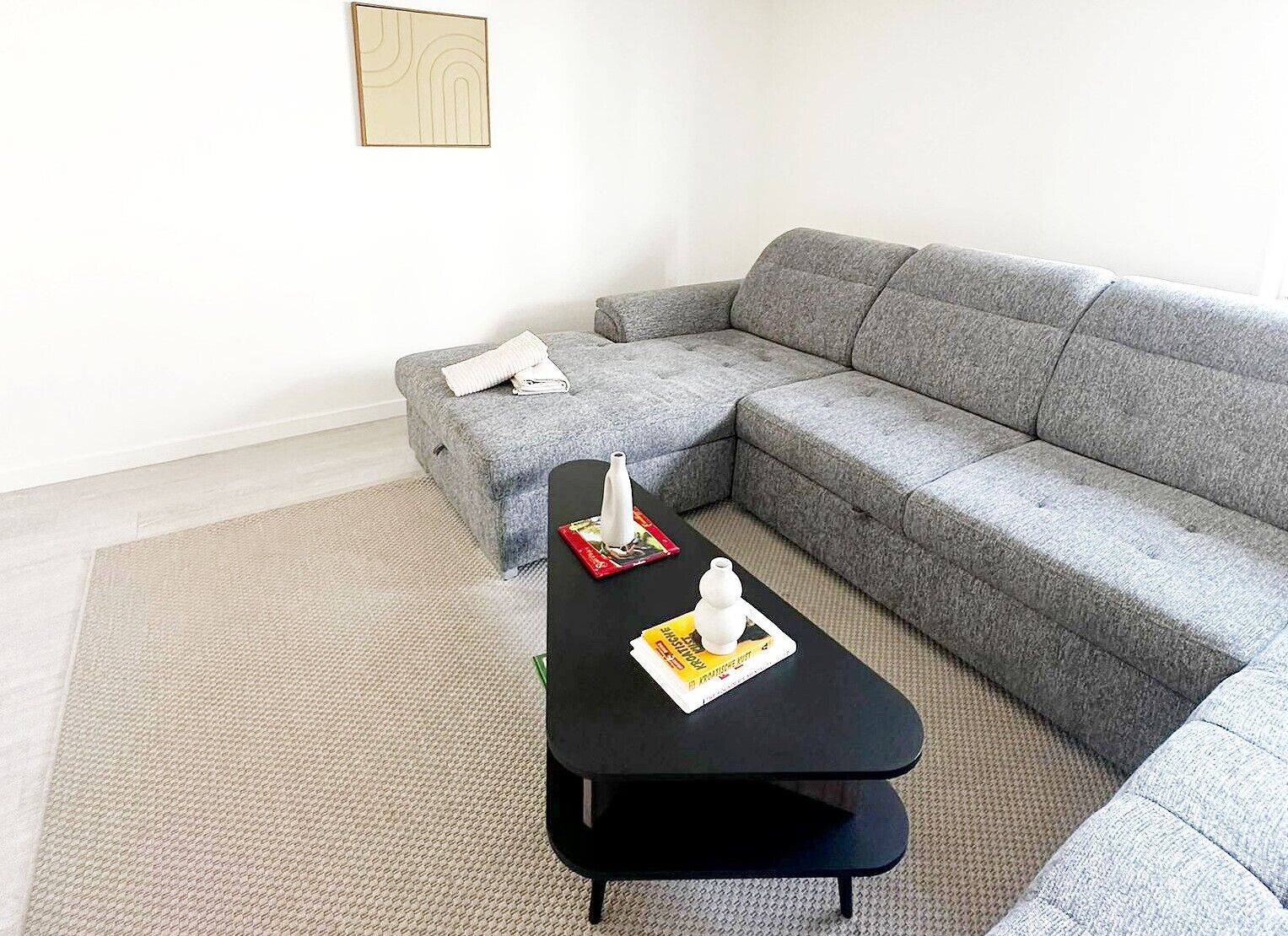 A modern living room with a grey sofa, a black coffee table, and a white wall art piece.