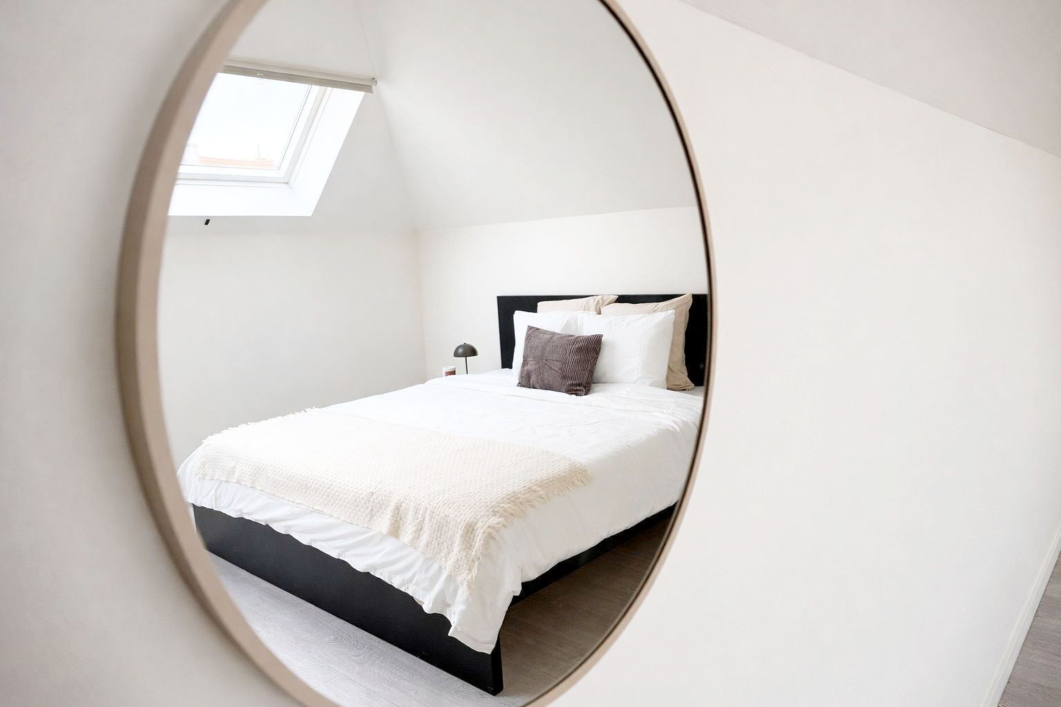 Een slaapkamer met een bed, nachtkastje, lamp en raam.