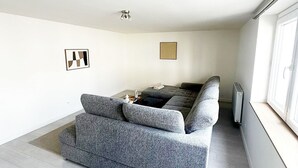 Un salon moderne avec un canapé gris, une petite table sur laquelle se trouve une bouilloire et un radiateur.