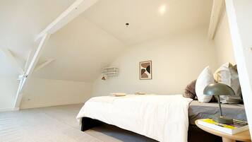 A bedroom with a bed, a bedside table with a lamp, a small shelf, and a wall-mounted light fixture.