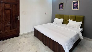 Une chambre à coucher avec un lit, un ventilateur de plafond, des spots encastrés, une porte en bois et deux tableaux encadrés accrochés au mur.