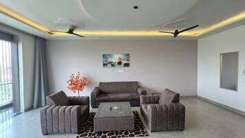 Uma sala de estar moderna com um conjunto de sofá, uma mesa de centro, um tapete estampado com girafas, ventiladores de teto e um quadro fixado na parede.