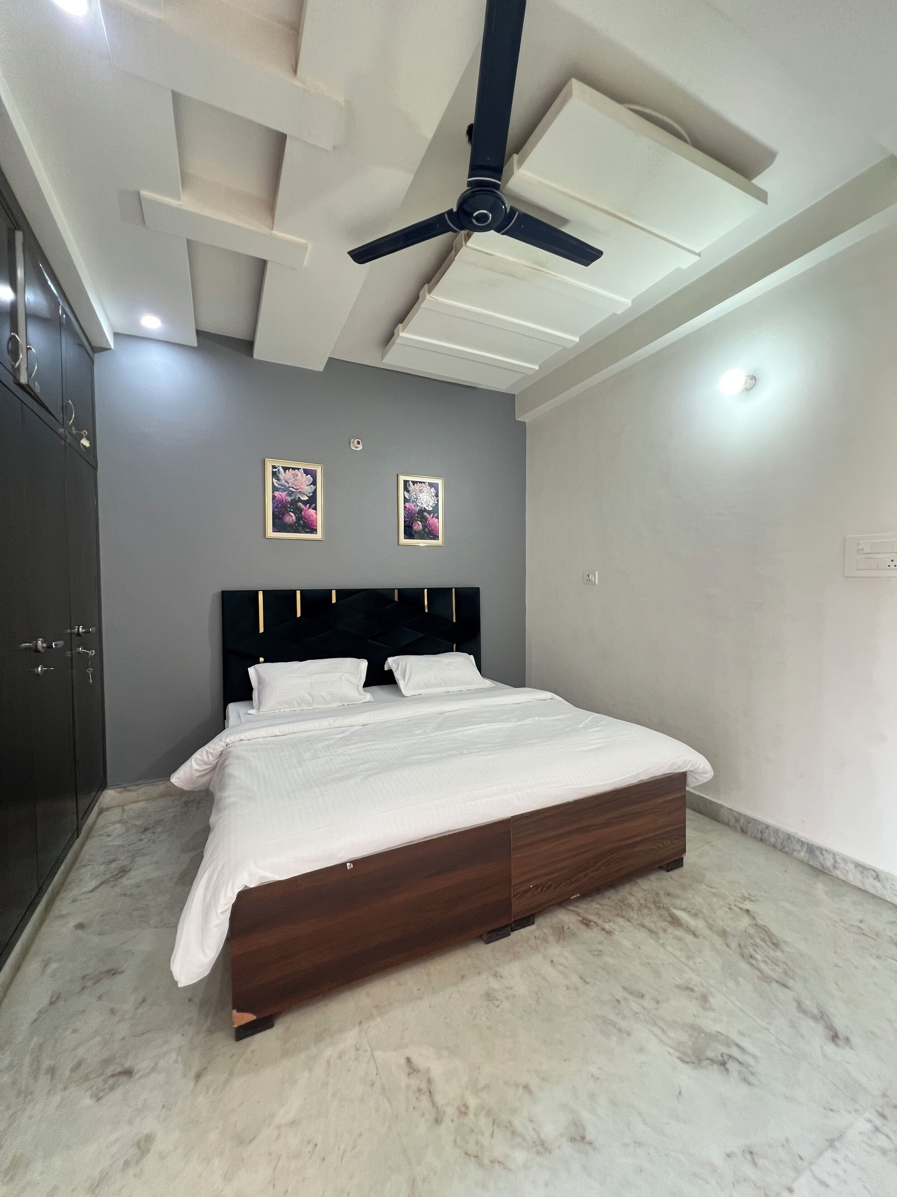 Ein Schlafzimmer mit einem Bett, einem Deckenventilator, eingelassener Beleuchtung und zwei gerahmten Blumenbildern an der Wand.