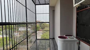 Een balkon met een metalen hekwerk, een wasmachine en een raam met een Carrier airconditioner.