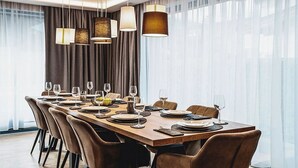 Un espace repas avec une longue table en bois, dressée pour six personnes, entourée de six chaises, et éclairé par des luminaires suspendus.