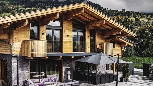 Une maison moderne en bois, dotée d’un balcon, d’un espace salon extérieur et d’un mur en pierre.