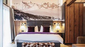 Une chambre avec un lit, un banc, une lampe fixée au mur et une vue sur la montagne.