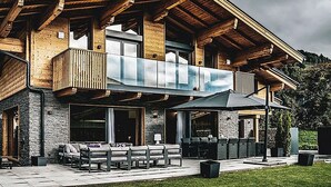 Une maison moderne à deux étages, dotée d’un balcon, d’un espace salon extérieur et d’une façade en pierre.