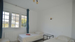 Ein Zimmer mit zwei Betten, einem kleinen Tisch, einem Heizkörper und einem Fenster mit Vorhängen.