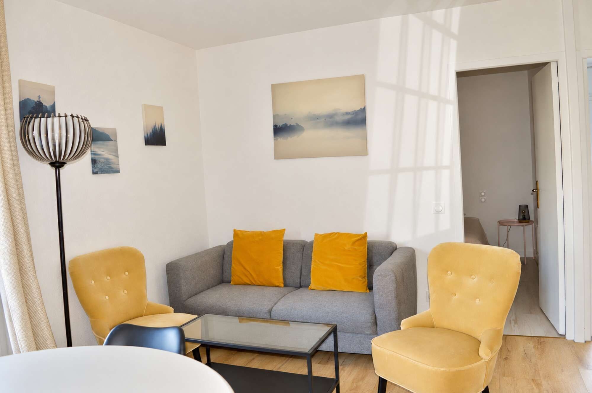 A living room with a grey sofa, two yellow armchairs, a glass coffee table, and a floor lamp.