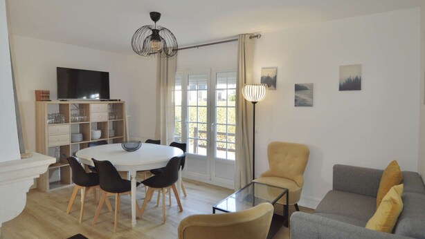 Ein modernes Wohnzimmer mit einem runden Esstisch, schwarzen Stühlen, einer Couch und einem Fernseher.