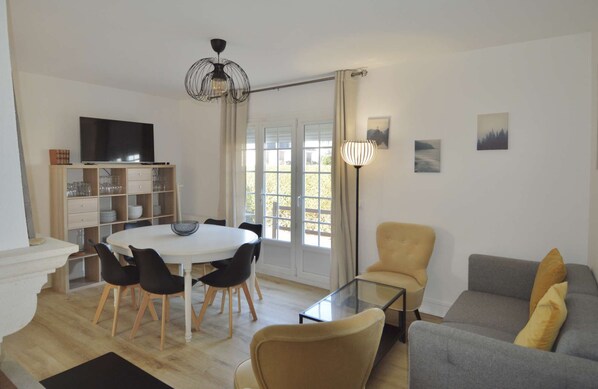 Ein modernes Wohnzimmer mit einem runden Esstisch, schwarzen Stühlen, einer Couch und einem Fernseher.