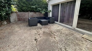 Un patio con mobili da esterno, pavimento in cemento, parete ricoperta di vegetazione e una porta a vetri scorrevoli.