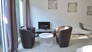 Una stanza moderna con TV, due divani, un tavolino rotondo e opere d'arte alle pareti.