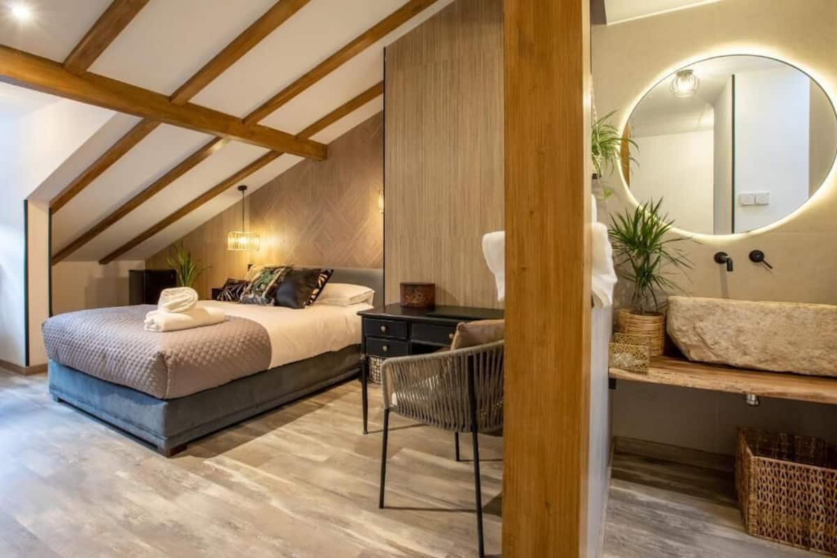 A bedroom with a bed, a desk, a chair, a round mirror, and a small plant.