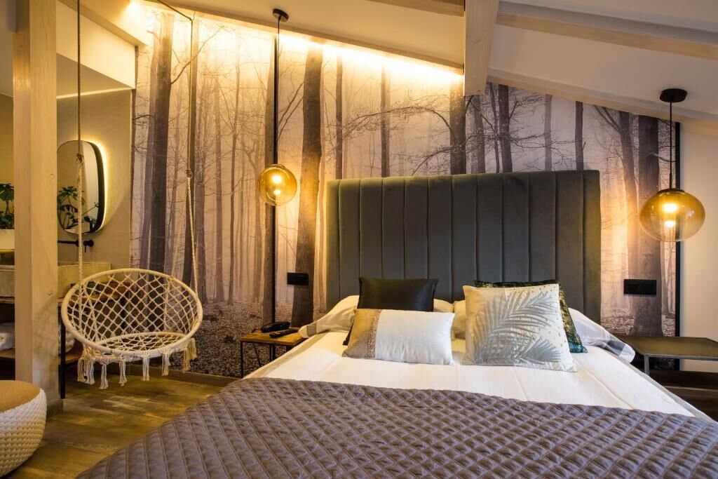 Une chambre à coucher moderne avec un grand lit, un fauteuil suspendu et une fresque murale sur le thème de la forêt.