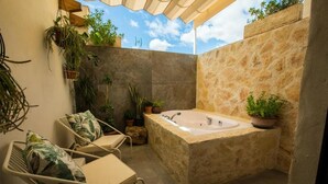 A stone bathtub in a corner, surrounded by potted plants and a white chair with a cushion. - La Posada de Consuelito (Chiloeches)