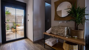 A modern bathroom with a large mirror, a wooden shelf with towels, a potted plant, and a view through a glass door to an outdoor area. - La Posada de Consuelito (Chiloeches)
