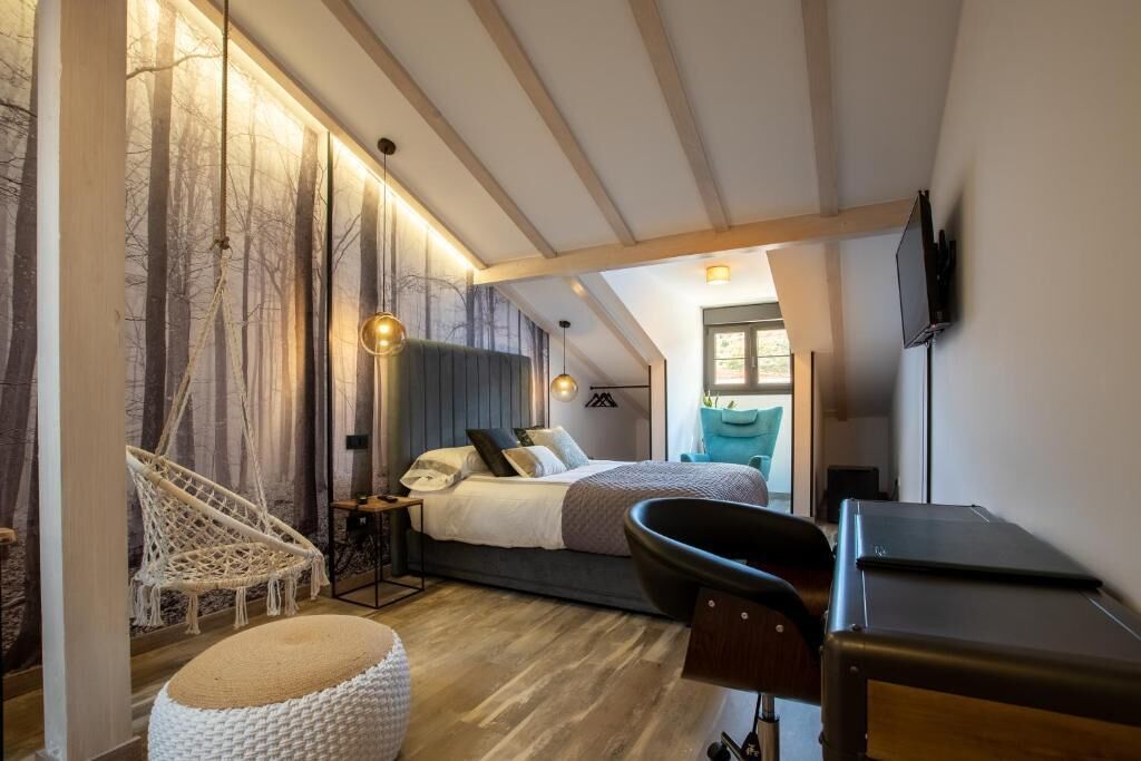Ein modernes Schlafzimmer mit Bett, Schreibtisch, Stuhl, einer Pendelleuchte und einem an der Wand montierten Fernseher.