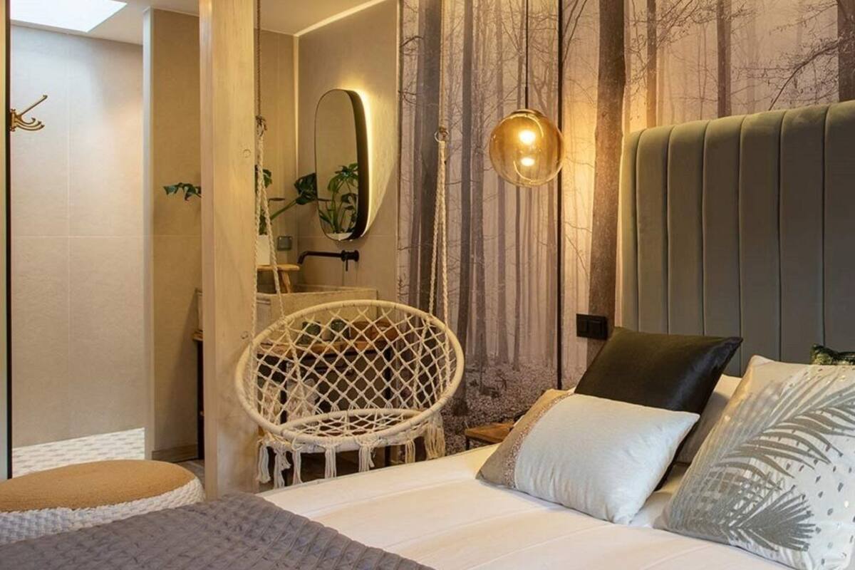 A bedroom with a bed, a hanging chair, a large mirror, and a wall with vertical lines.
