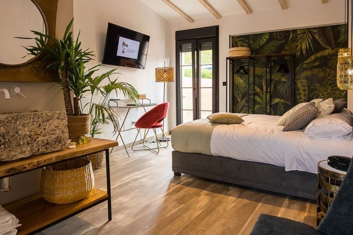 A bedroom with a bed, a TV, a desk, a chair, and a large window.
