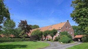 En stor murstensbygning med rødt tegltag, omgivet af velholdte græsplæner og træer.