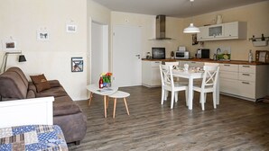 En kompakt opholdsstue med sofa, spisebord med stole, et køkkenområde med mikroovn og skabe, samt en dør til et andet rum.