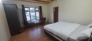 A bedroom with a bed, a desk, a chair, a wardrobe, and a window. - Orion Home (Leh)