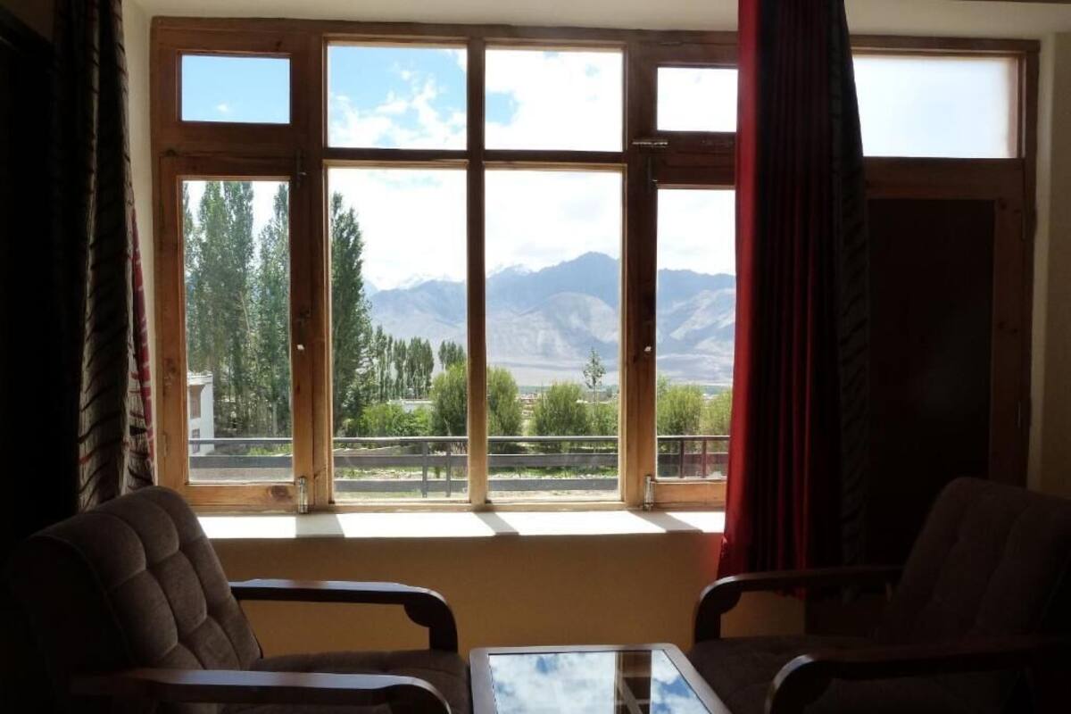 A room with a large window, two chairs, a small table, and a view of mountains.