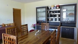 Zona pranzo con tavolo e sedie in legno, cucina con mobili e scaffali, e una porta che dà su un'altra stanza.