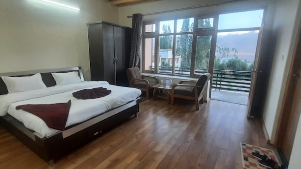 Una camera d'albergo con un letto, un armadio, un tavolino con sedie e un balcone con vista.