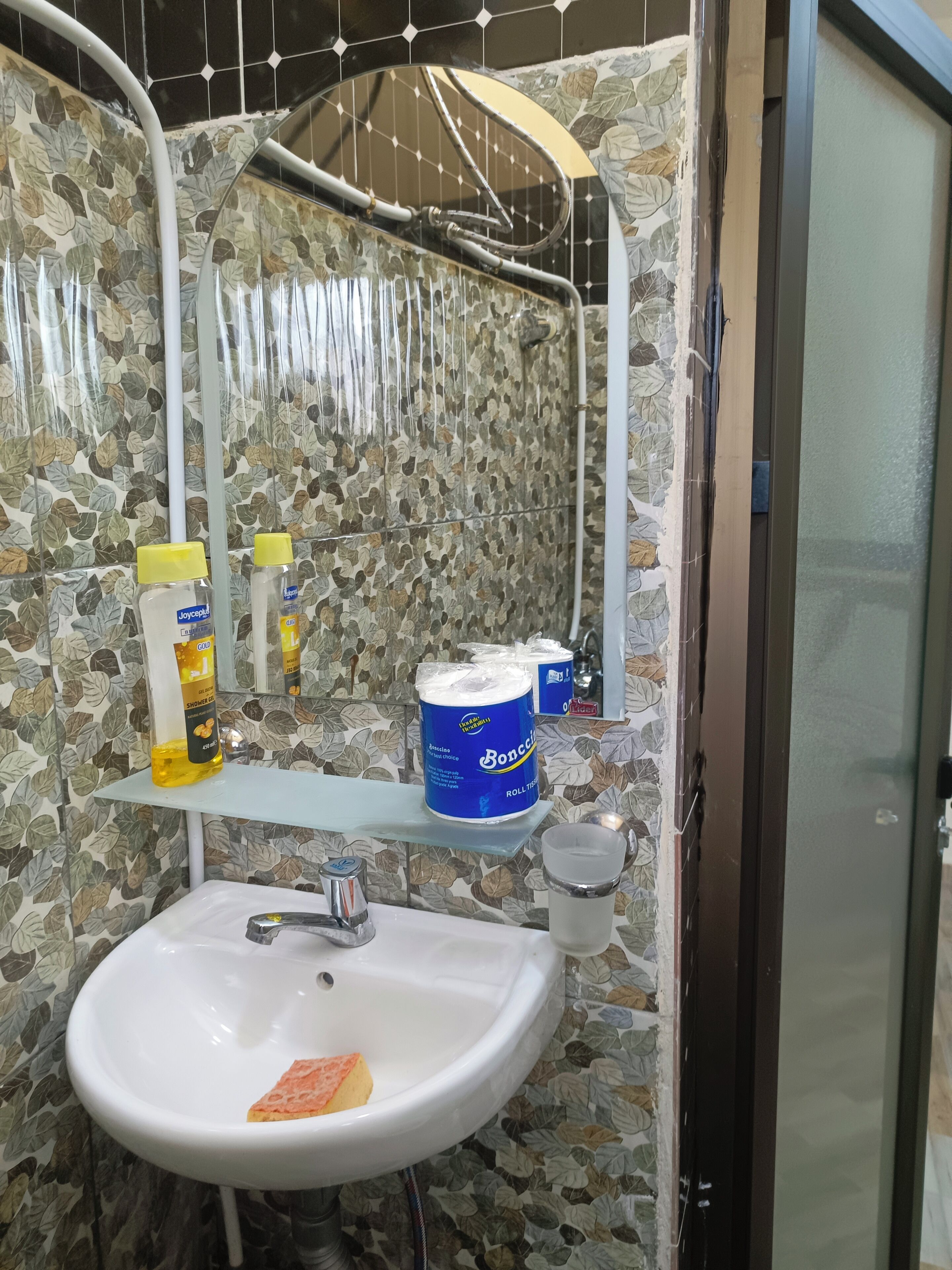 Un baño con lavamanos blanco, ducha y estante con artículos de aseo.