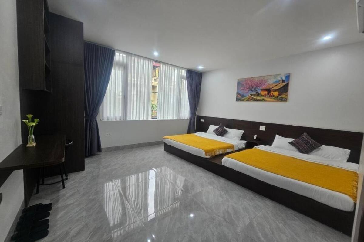 A hotel room with two beds, a desk, a chair, a painting on the wall, and a window with curtains.