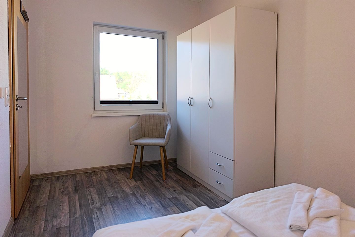 Ein Schlafzimmer mit Bett, Stuhl, Kleiderschrank und Fenster.