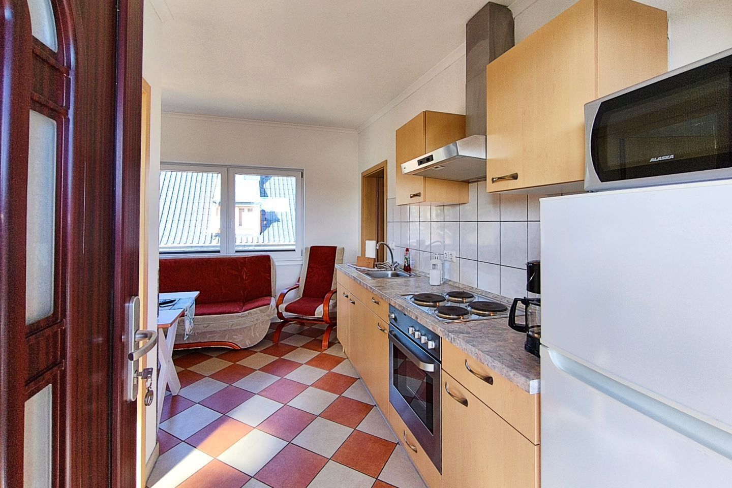A compact kitchen with a stove, microwave, and a dining area with a red chair and a table.