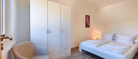 Un dormitorio con cama, una silla, un armario y una mesita de noche con lámpara.