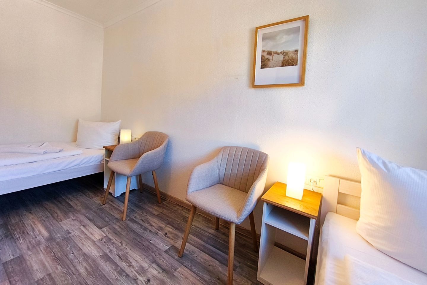 Une chambre d’hôtel avec un lit, deux fauteuils, une table de chevet avec une lampe et un tableau encadré au mur.