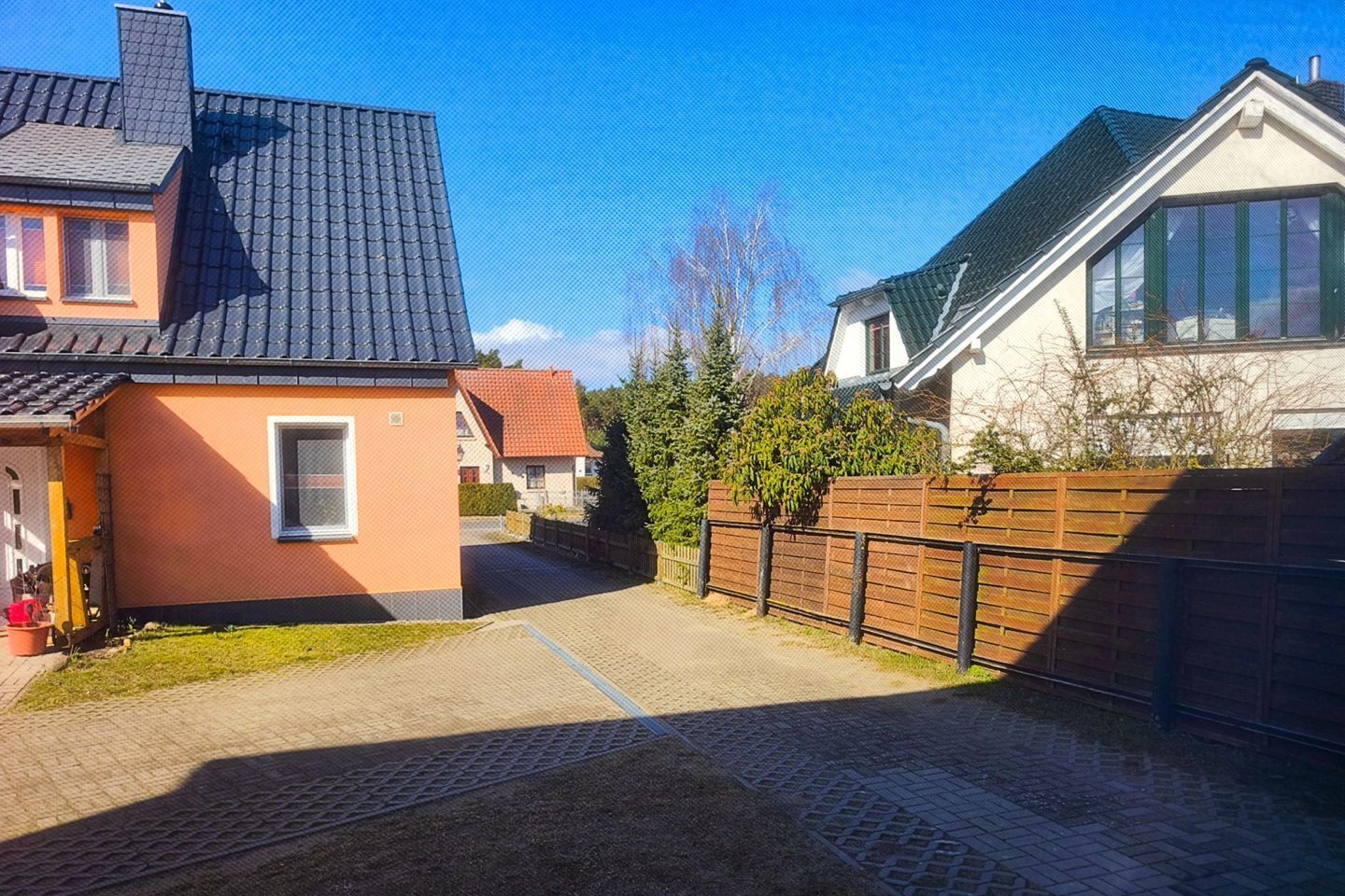 A residential street with houses, a paved driveway, and a wooden fence.
