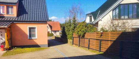 A residential street with houses, a paved driveway, and a wooden fence.