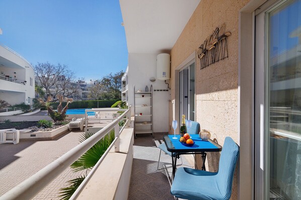 A balcony with a table, chairs, and a view of a pool and buildings.