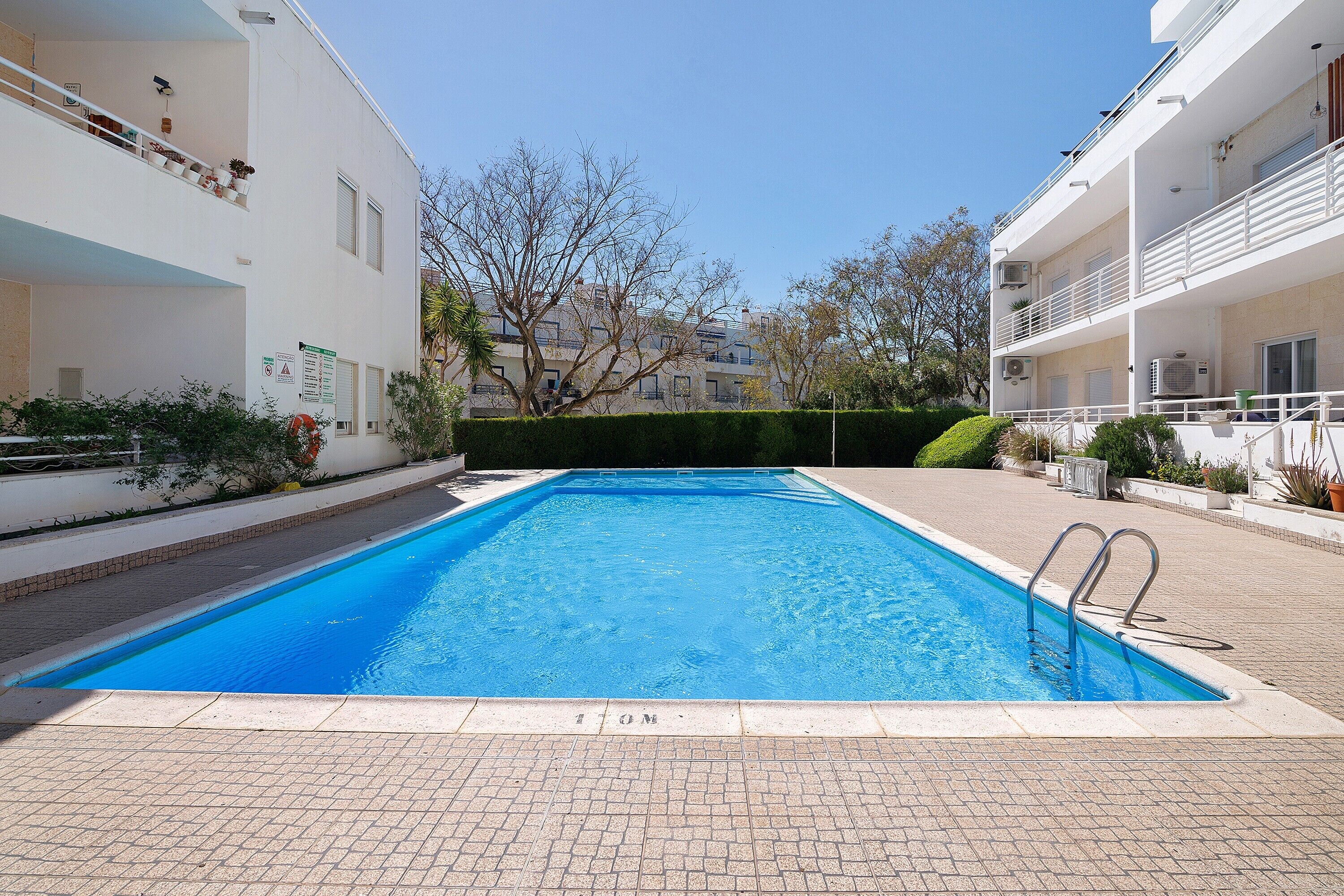 A rectangular swimming pool with a clear blue surface, surrounded by a paved walkway.