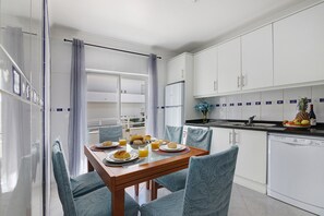 A dining area with a table set for breakfast, a kitchen with white cabinets, and a view through a glass door.