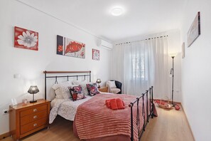 A bedroom with a bed, bedside table, lamp, and artwork on the wall.