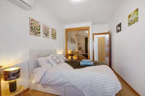 A bedroom with a bed, a bedside lamp, wall art, and a mirror.