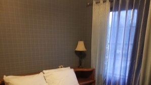 A bedroom with a bed, a nightstand, a lamp, and a window with curtains. - HIdden Gem (Wallkill)
